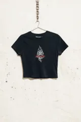 Baby tee negra de manga corta, corte ajustado y tiro corto (crop top), con estampado frontal de una rosa estilizada con llamas y texto en rojo.