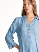 Blusa de lyocell color azul claro, con cuello camisero, escote en V y abertura frontal con tres botones. Mangas 3/4 amplias.