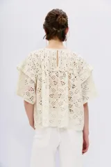 Blusa blanca de broderie con escote redondo, mangas cortas con volados en sisa y detalle de alforzas en el canesú.