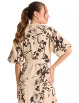 Vestido maxi de crepe color beige con estampado floral en tonos marrones y negros. Presenta cuello a la base, escote en V, abertura central con botones y cintura con lazo de ajuste y hebilla.