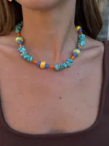 Collar corto con piedras turquesas irregulares, cuentas de cerámica amarillas y verdes, y cuentas plásticas naranjas y azules.