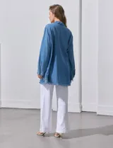 Camisa de jean celeste, marca Hester & Orchand, de corte oversize con cuello con solapa, escote en V y abertura central con botones. Delantera con bolsillos aplicados, mangas largas regulables con presilla y botón, y ruedo desflecado.