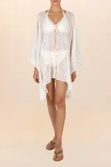Salida de playa corta tipo poncho en color blanco marfil, confeccionada en algodón ligero y traslúcido. Presenta escote en V con lazo frontal ajustable terminado en borlas y detalles bordados en tono crema.