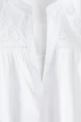 Blusa blanca de algodón con corte holgado, cuello mao y mangas cortas con volados. Presenta broderie en el canesú delantero.