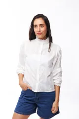 Camisa blanca de algodón con cuello alto con volados, mangas largas abullonadas y cierre frontal con botones.