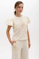Blusa color crema de lino con bordado en relieve de forma floral y mangas cortas con volados.
