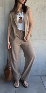 Conjunto sastrero tostado con rayas verticales finas, compuesto por un pantalón de corte recto y un chaleco sin mangas con solapas. El pantalón tiene cierre frontal con botón y bolsillos laterales. El chaleco tiene un botón frontal y bolsillos simulados.