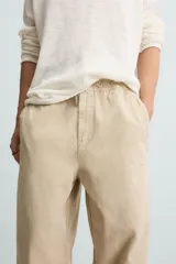 Pantalón de algodón color beige con efecto lavado, corte relajado y pierna ancha. Presenta cintura elástica con ajuste de cordón y cierre frontal con botón, además de bolsillos delanteros y bolsillos traseros de plastrón.