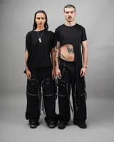 Pantalón negro de corte holgado con múltiples correas y ojalillos metálicos.