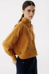 Camisa azul de lino con cuello clásico, manga larga y cierre frontal con botones. Presenta bordados de dados, cartas y el nombre de la marca.