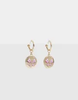 Aros tipo argolla dorados con dije colgante circular con moño esmaltado rosa y apliques de strass.