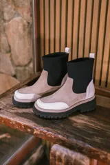 Bota de cuero color beige con caña de neopreno negra, suela track color negro y tirador trasero.