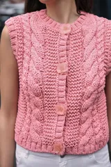 Chaleco tejido de punto color rosado, con cuello redondo y sin mangas. Cierre frontal con botones a presión en forma de flor.
