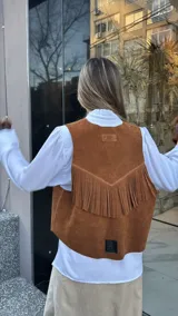 Chaleco marrón de cuero descarne con terminación en picos, tachas metálicas y flecos en la espalda.