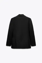 Blazer negra de corte clásico, con cuello de solapa y escote en pico. Tiene mangas largas con hombreras, bolsillos con solapa en el delantero y un bolsillo de vivo en el pecho. Está forrada y se cierra con un botón frontal.