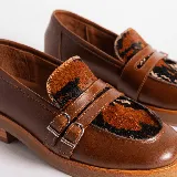 Mocasines de cuero color marrón con estampado de cocodrilo, detalle de hebilla metálica plateada y suela de goma negra. Diseño clásico con punta redonda y calce cómodo.