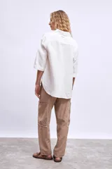 Camisa blanca de manga tres cuartos, con cuello camisero y corte holgado. Presenta un bolsillo de parche en el pecho izquierdo.