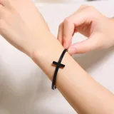 Brazalete rígido abierto de acero quirúrgico color negro con dije de cruz.