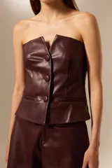 Top sin mangas de cuero sintético color borgoña, con cuello strapless, pinzas en el busto y cierre frontal con tres botones grandes.