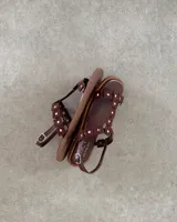 Sandalias chatas de cuero vacuno color marrón con tiras con apliques de tachas doradas.