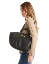 Cartera tote negra de ecocuero con base redondeada y pliegues decorativos. Cuenta con una solapa central con herraje dorado en forma de "T" y asas dobles para hombro y mano. El interior tiene triple compartimento.