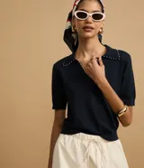 Blusa de punto color blanco, con cuello polo, escote en V y mangas cortas. Detalle de mini perlas aplicadas en el cuello.