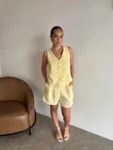 Conjunto de dos piezas color rojo vibrante, compuesto por un chaleco sin mangas con escote en V y botones frontales, y un short de tiro alto con pliegues y bolsillos laterales.