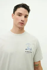 Remera azul de manga corta con cuello redondo y estampado de sombrilla, reposera, balde y pala de playa.