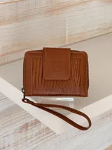 Billetera marrón de cuero con textura croco, cierre de cremallera y correa de muñeca. Presenta un broche con el logo de un búho.