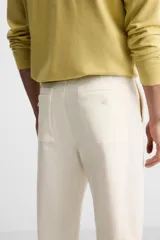 Pantalón chino color crema de corte recto, confeccionado en tejido de algodón con elasticidad. Cuenta con bolsillos frontales y traseros de plastrón con botón. Cierre frontal con cremallera y botón.
