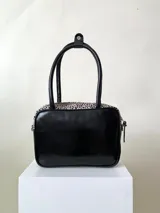 Cartera rígida negra de cuero con tachas plateadas y tres combinaciones de cuero diferentes que aportan textura. Tiene herrajes y cierre metálico plateado marca YKK. Cuenta con un asa fina para llevar al hombro o en la mano y una correa larga extra regulable.