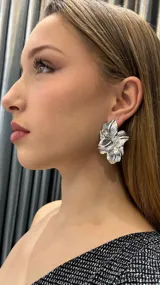 Aros tipo caravana con forma de flor plateada con textura y detalles de strass.