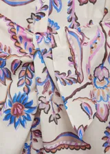 Vestido midi de corte camisero con estampado floral en tonos rosa, azul y marrón sobre fondo blanco. Tiene cuello mao, mangas 3/4 con puños abotonados, cierre frontal con botones y lazo decorativo en la cintura.