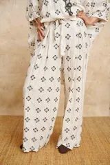 Pantalón palazzo color crudo con bordado de flores negras y cinto de lazo.