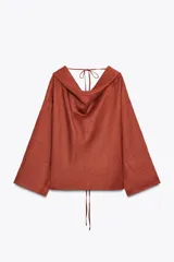 Blusa color ladrillo confeccionada en lino 100%. Tiene cuello fluido, mangas largas acampanadas y espalda descubierta ajustable con cordones.