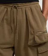 Bermuda masculina color verde oliva, confeccionada en algodón con felpa. Presenta cintura con lazo ajustable y bolsillos cargo laterales con cierre de cremallera.