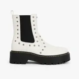 Bota blanca de caña media con elásticos laterales negros, plataforma track y detalle de tachas plateadas.
