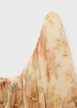 Blusa corta de gasa color crema con estampado floral en tonos durazno y verde. Tiene escote cuadrado, mangas largas abullonadas y espalda abierta.