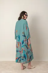 Vestido largo de lino color verde militar con estampado de hojas en tonos azul, naranja y marrón. Tiene cuello mao con botones, mangas tres cuartos y un bolsillo en el pecho.