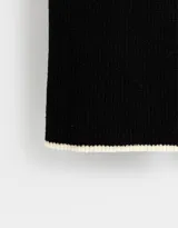 Bufanda larga de tejido de punto color negro con borde blanco y etiqueta de tela con logo en un extremo.