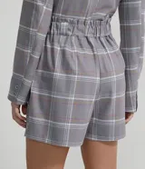 Short sastrero gris con estampado a cuadros blancos, amarillos y rosados. Tiene cintura media, pliegues, bolsillos y cierre frontal con cremallera.