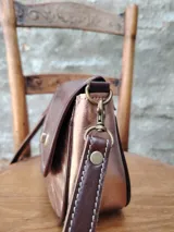 Bandolera color cobre con textura craquelada, solapa con cierre metálico y correa larga de cuero marrón.