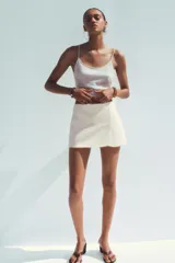 Falda pantalón corta color crema, de tiro medio con abertura en el delantero y cierre lateral con cremallera.