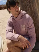 Buzo con capucha color lila, de algodón y fit relajado. Presenta un estampado con una palmera y el texto "Rainbow Bay" en el pecho.