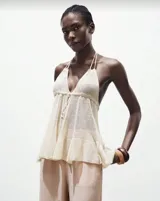 Top tejido color crudo, con breteles finos y corte holgado con volados en el ruedo.