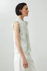 Camisa sin mangas color verde agua con cuello mao, cierre frontal con botones y detalle de puntilla en los hombros.