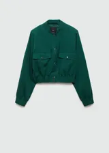 Chaqueta bomber verde esmeralda de lino y lyocell, con cuello redondo, cierre frontal con botones a presión, cintura y puños elásticos, dos bolsillos de parche con solapa en el pecho y corte cropped.