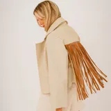 Chaqueta corta color beige de cuero, con cuello clásico, cierre frontal con botones y flecos de cuero marrón en la parte superior de la espalda.