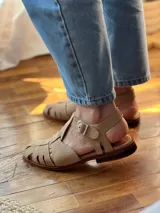 Sandalias de cuero color beige con diseño de tiras entrecruzadas y hebilla lateral.
