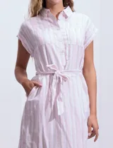 Vestido camisero corto con estampado de rayas verticales celestes y blancas. Tiene cuello camisero, mangas cortas con dobladillo, cierre frontal con botones y cinturón de lazo en la cintura.